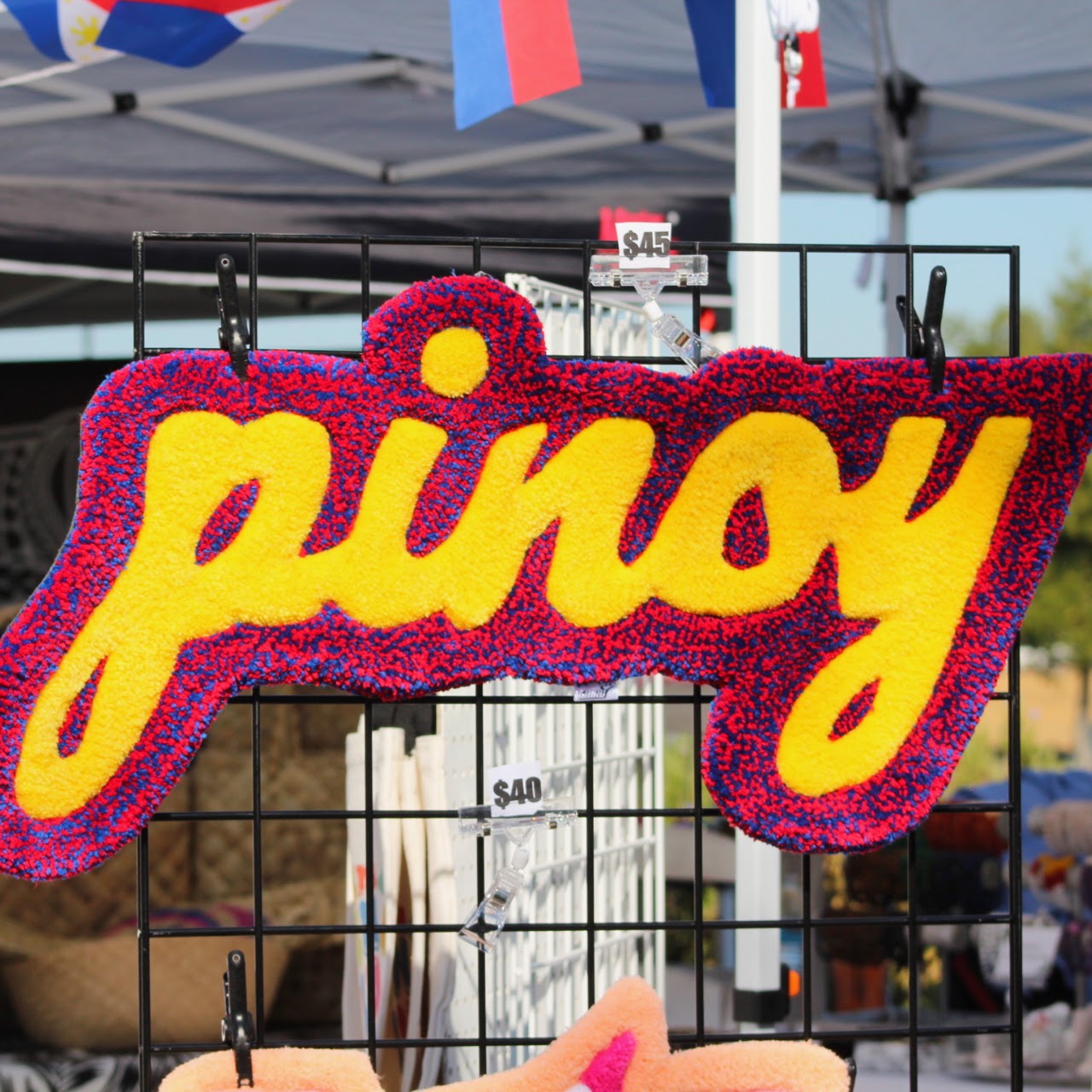 A bright red, blue, and yellow Pinoy sign displayed at a vendor booth.